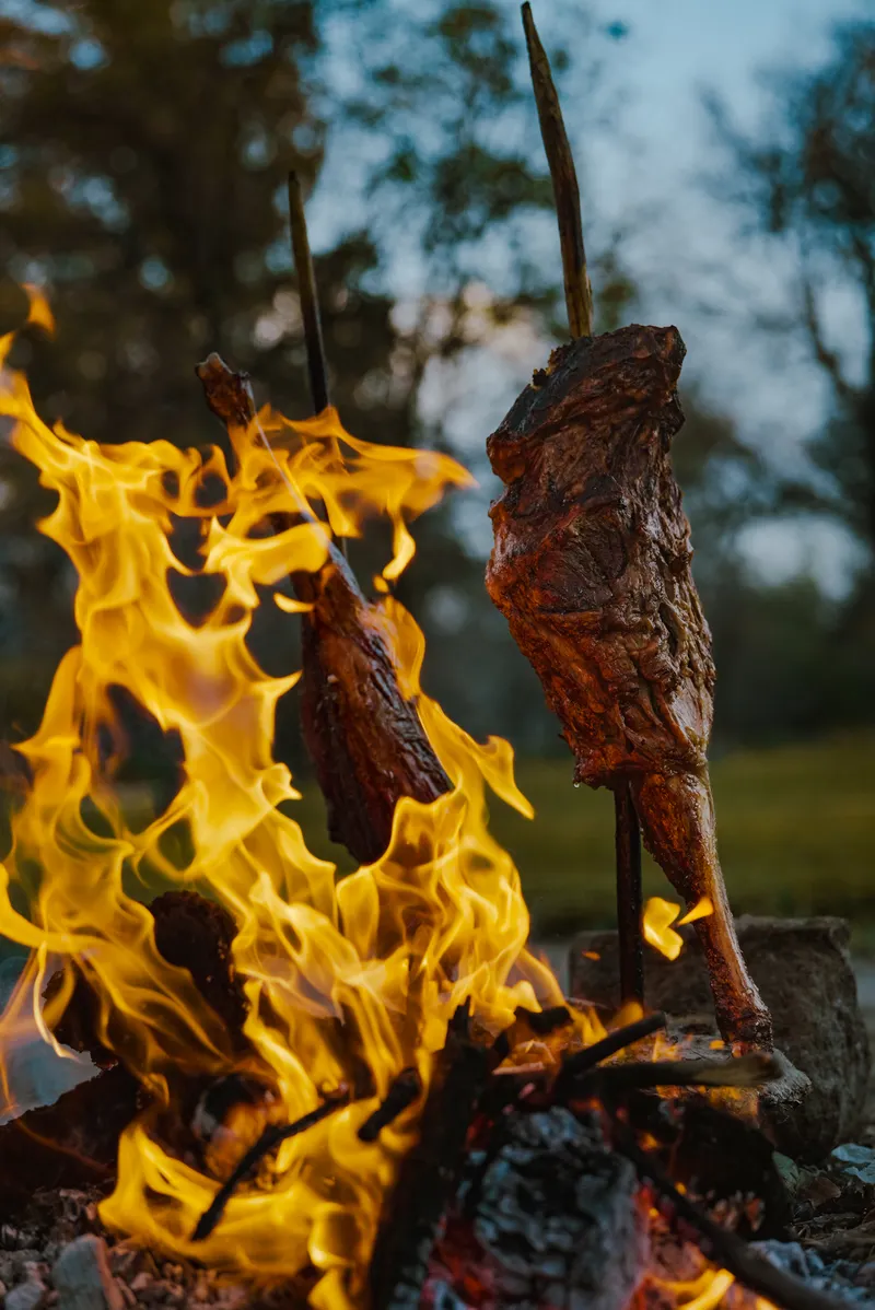 Carne ensartada asándose lentamente junto al fuego de leña