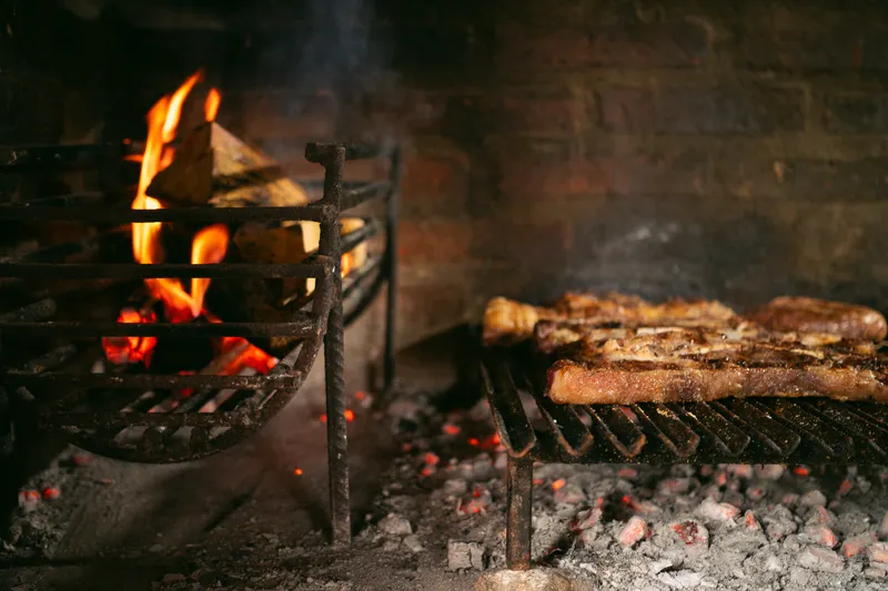 Fogón con leña encendida y carne asándose sobre la parrilla